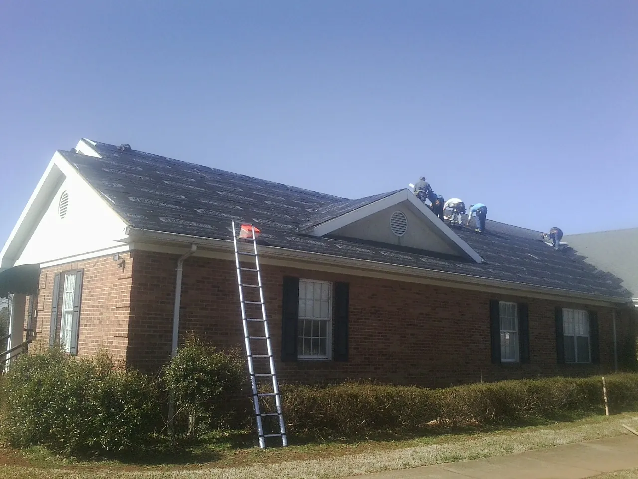 Crew tearing shingles off a brick ranch roof with a ladder set — Emergency Roof Repair work by our crew in Inwood