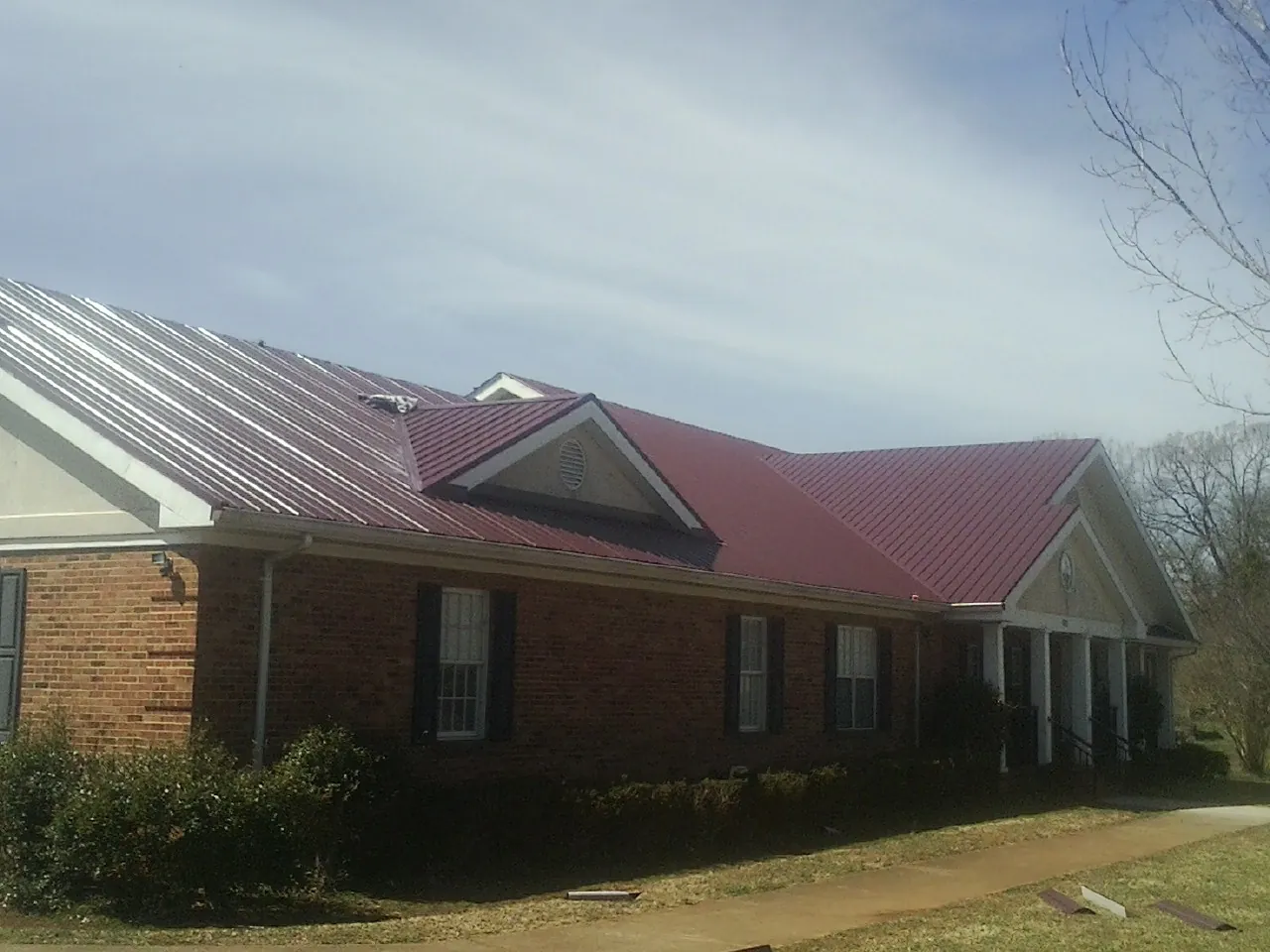 Red metal roof with gabled entries on a long brick building, from a Hail Damage Roof Repair job in Inwood