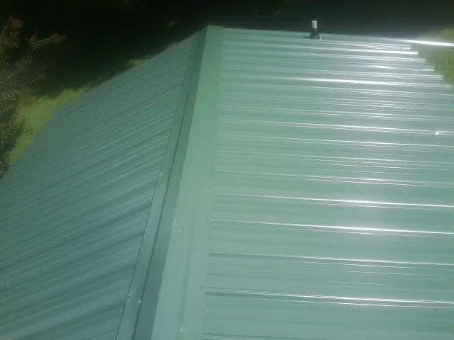 New green metal panels meeting at the ridge of a roof — Flat Roof Repair work by our crew in Inwood