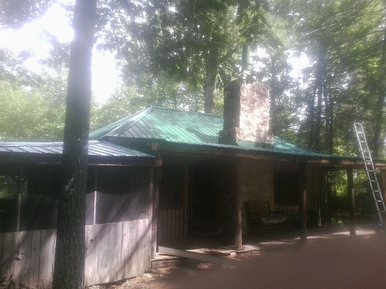 Green metal roof and stone chimney above a log cabin porch in Inwood